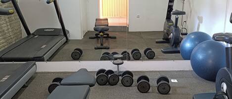 Un gimnasio con cintas de correr, mancuernas, un banco y pelotas de ejercicio.