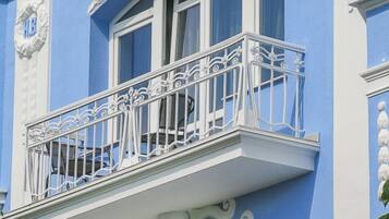 En bygning med en blå facade, en balkon med detaljerede hvide gelændere og dekorative hvide arkitektoniske detaljer.