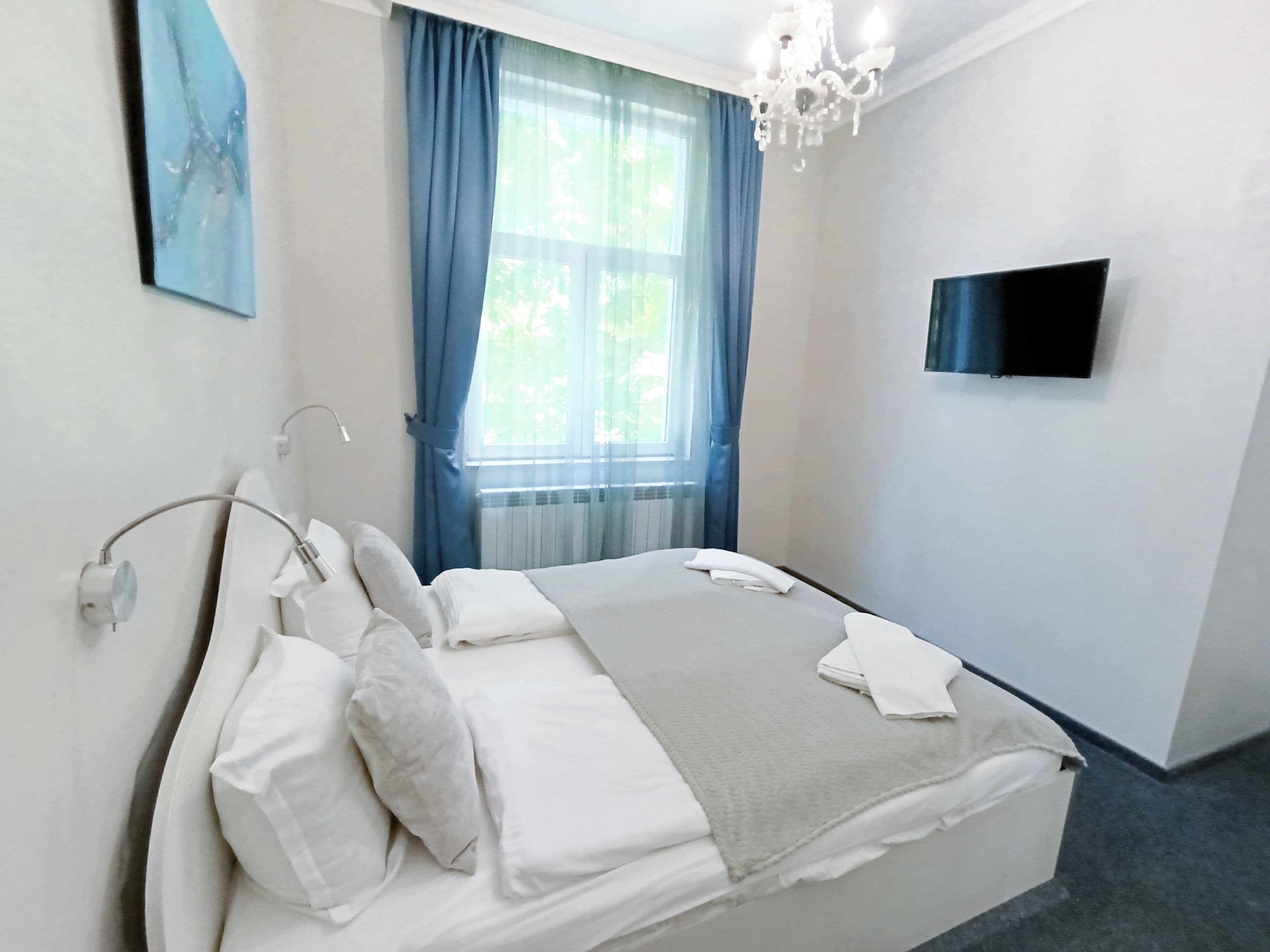 Un dormitorio con cama, televisor en la pared y ventana con cortinas.