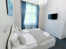 A bedroom with a bed, a television on the wall, and a window with curtains.