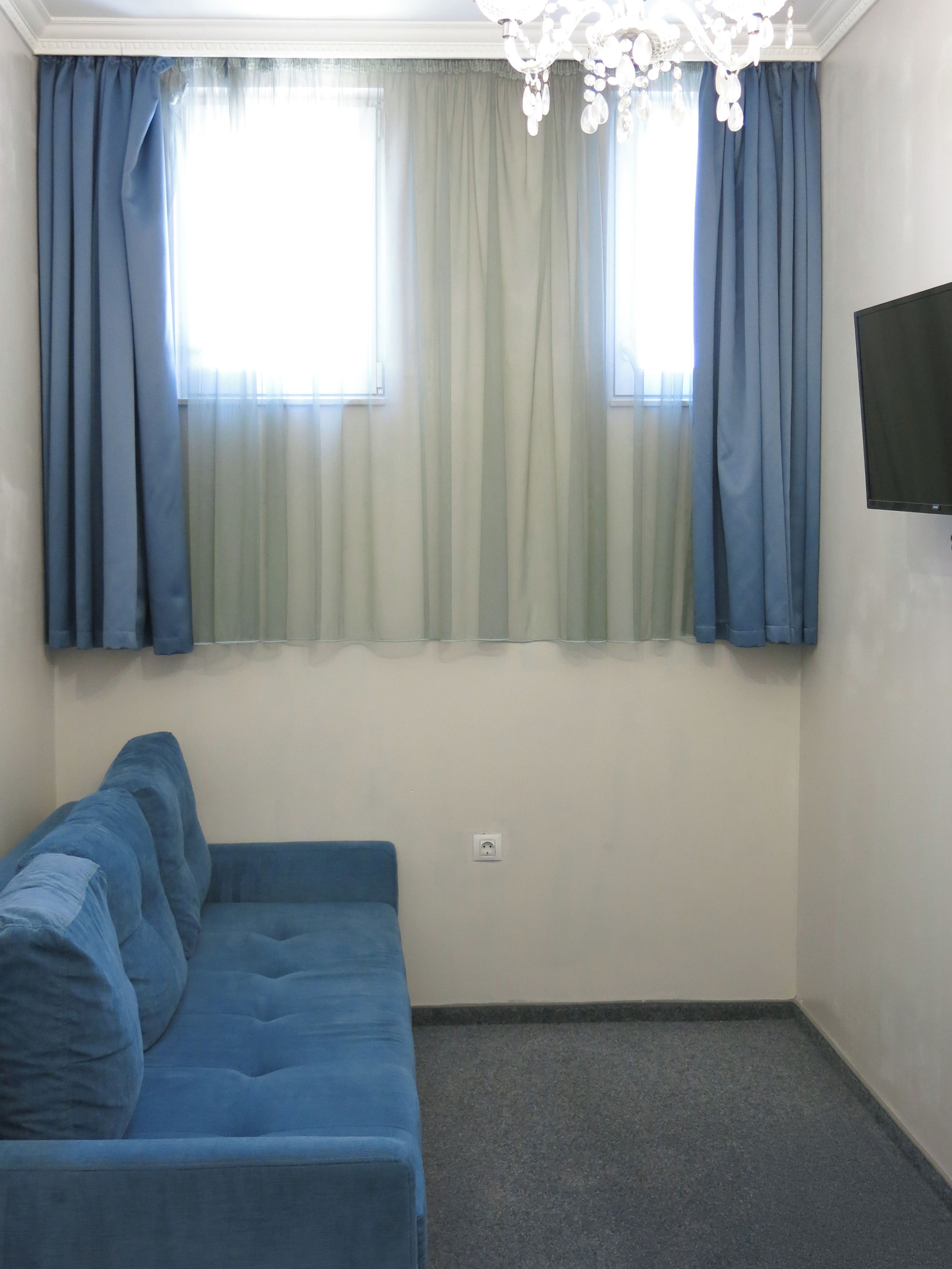 A room with a blue sofa, a television mounted on the wall, and a window with curtains.