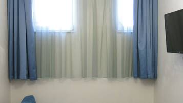 A room with a blue sofa, a television mounted on the wall, and a window with curtains.