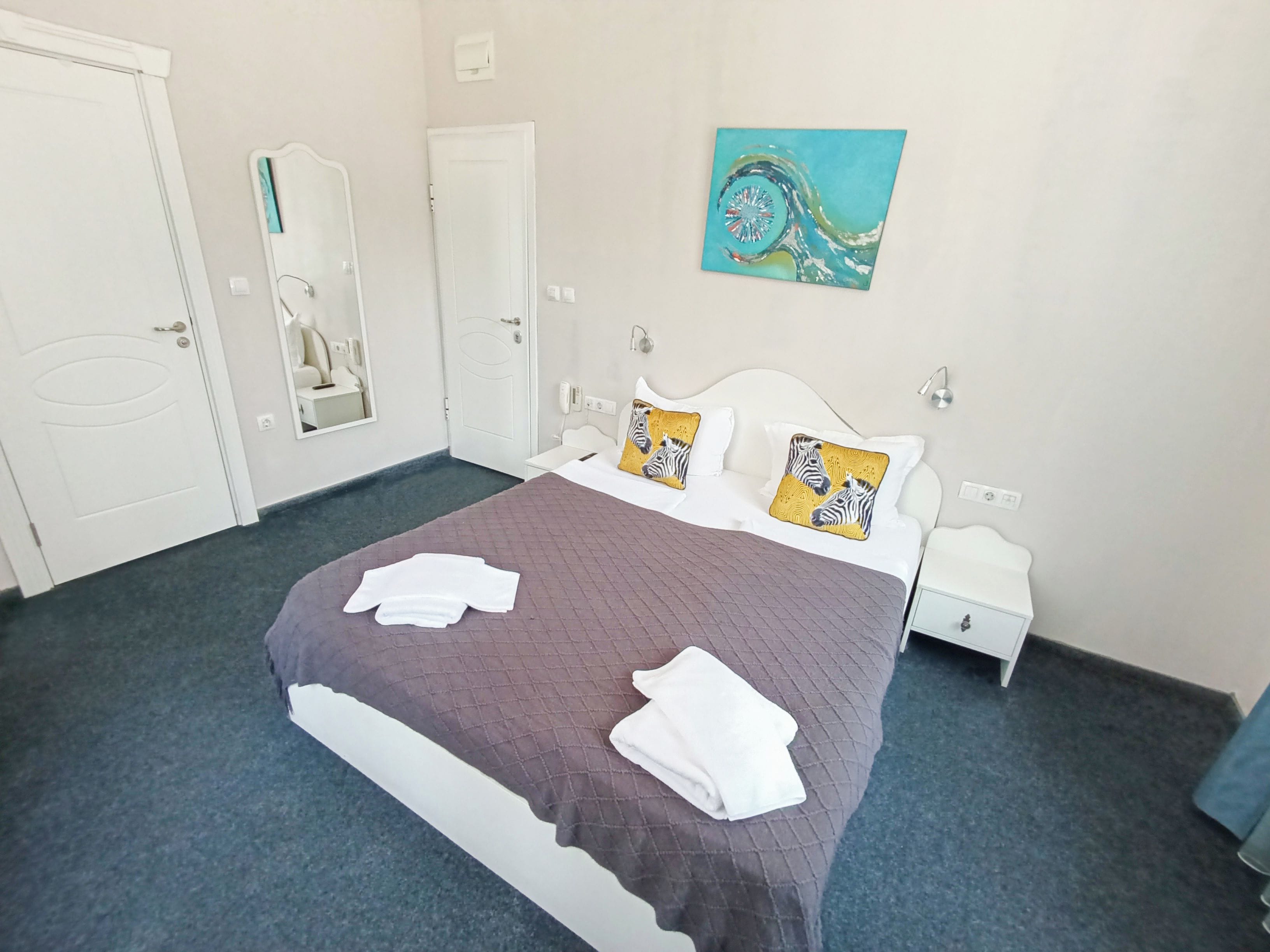 Una habitación de hotel con cama, dos mesitas de noche, un espejo y un cuadro en la pared.