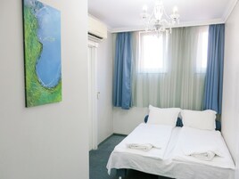 Una habitación de hotel con una cama, un candelabro, un cuadro y un ventanal con cortinas.