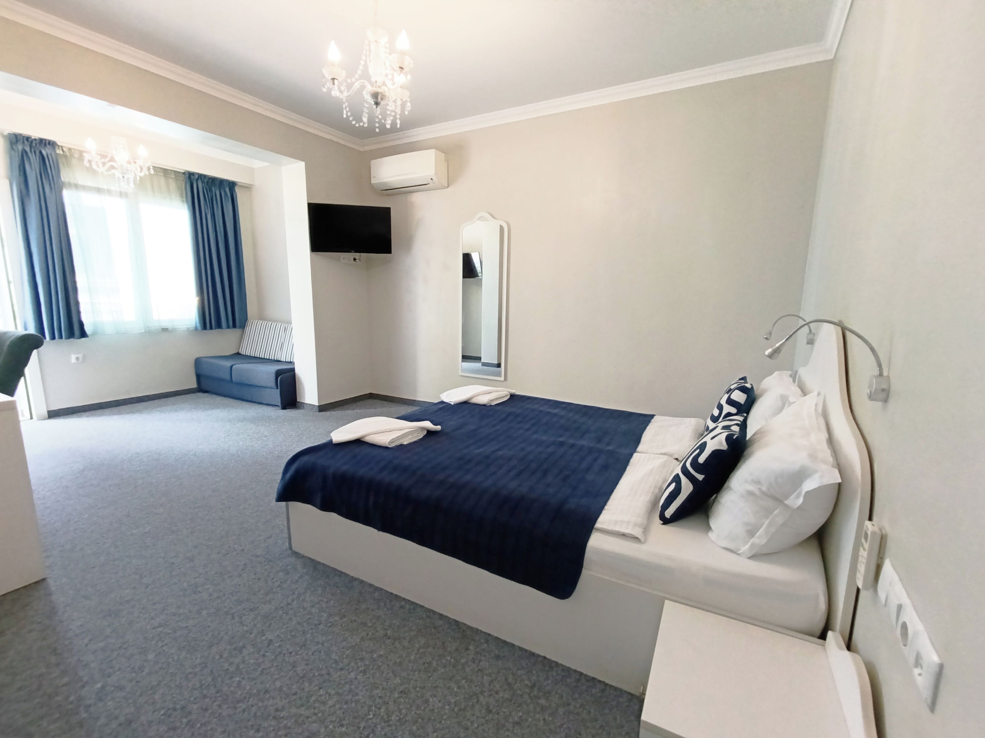Habitación de hotel con cama, escritorio, silla, televisión y ventana con cortinas.