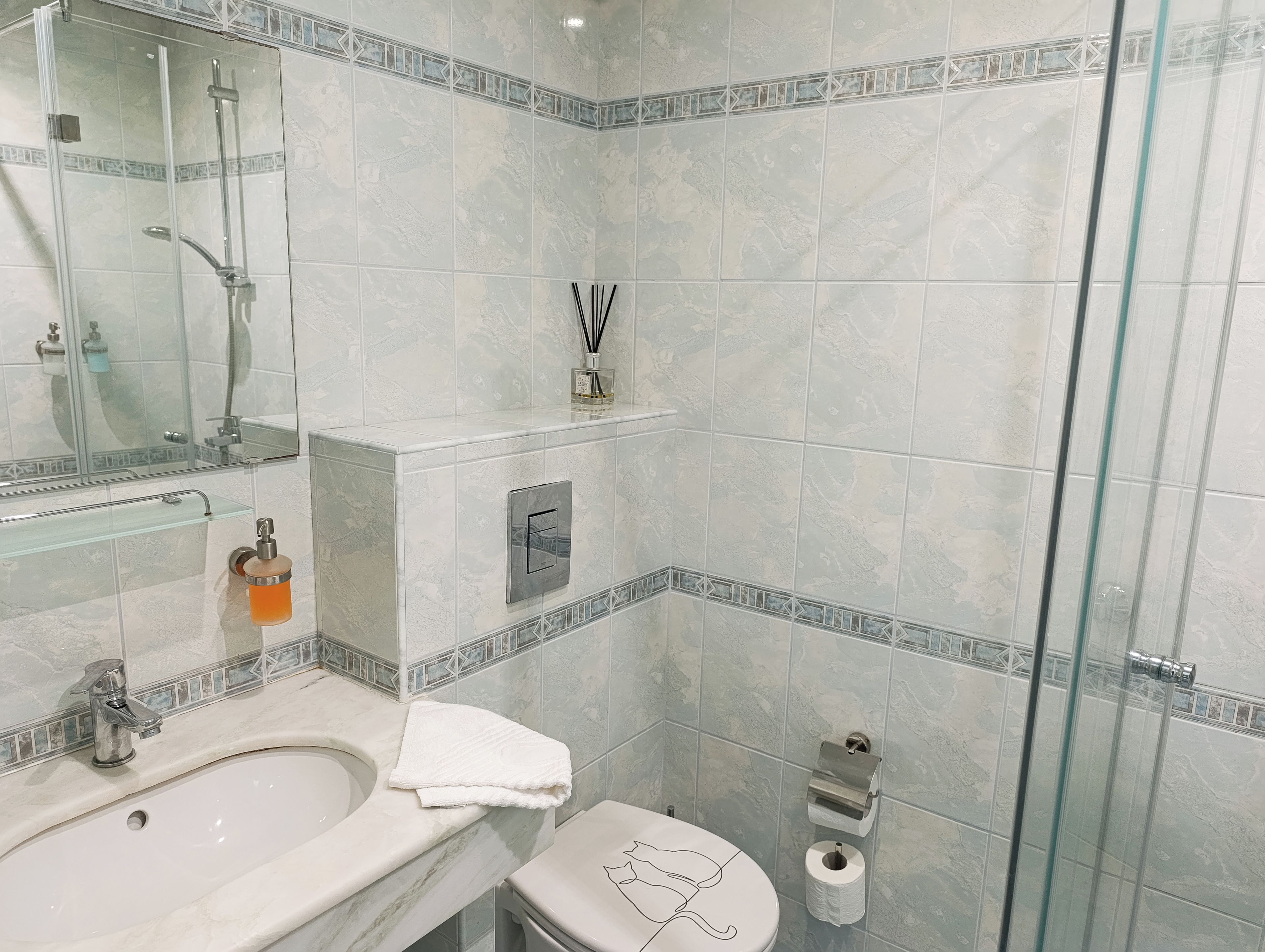 Un baño con cabina de ducha de vidrio, un lavamanos, un inodoro y un perchero para toallas.