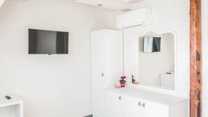 Un baño blanco con una televisión montada, un espejo grande y un armario blanco.