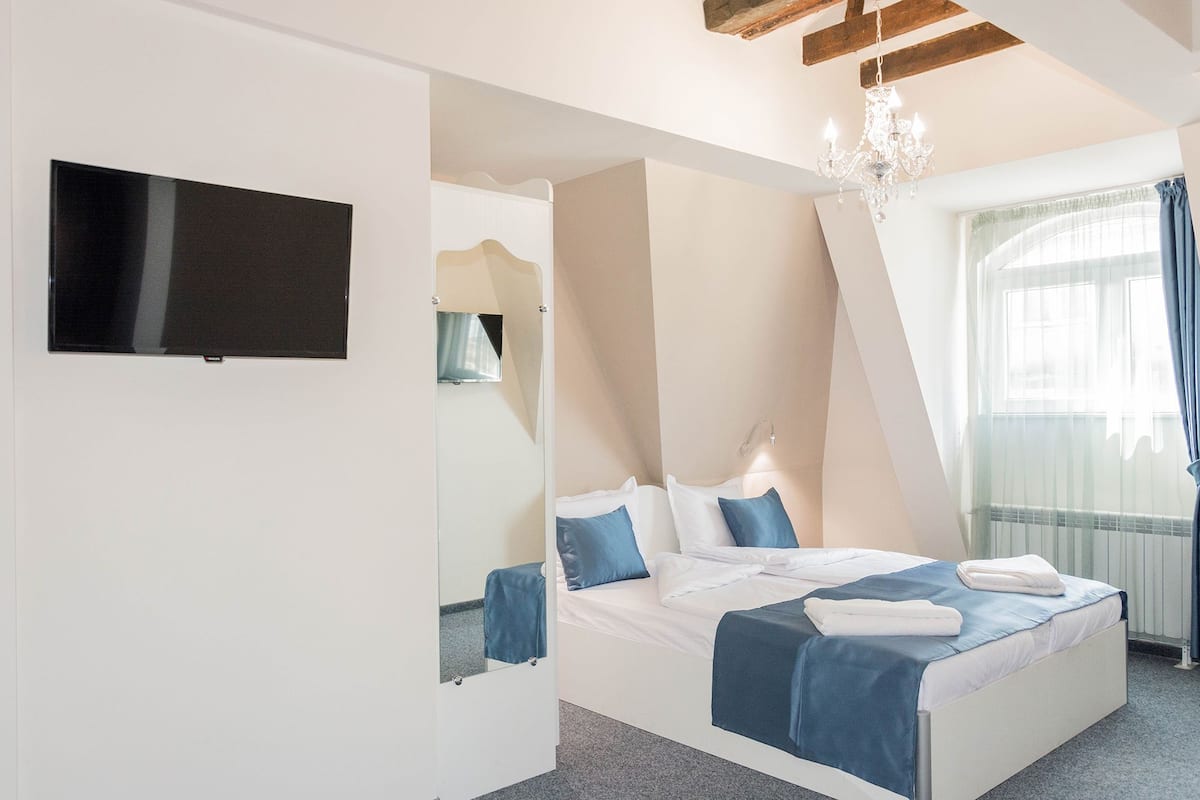 Un dormitorio con cama, televisor, candelabro y ventana con cortinas.