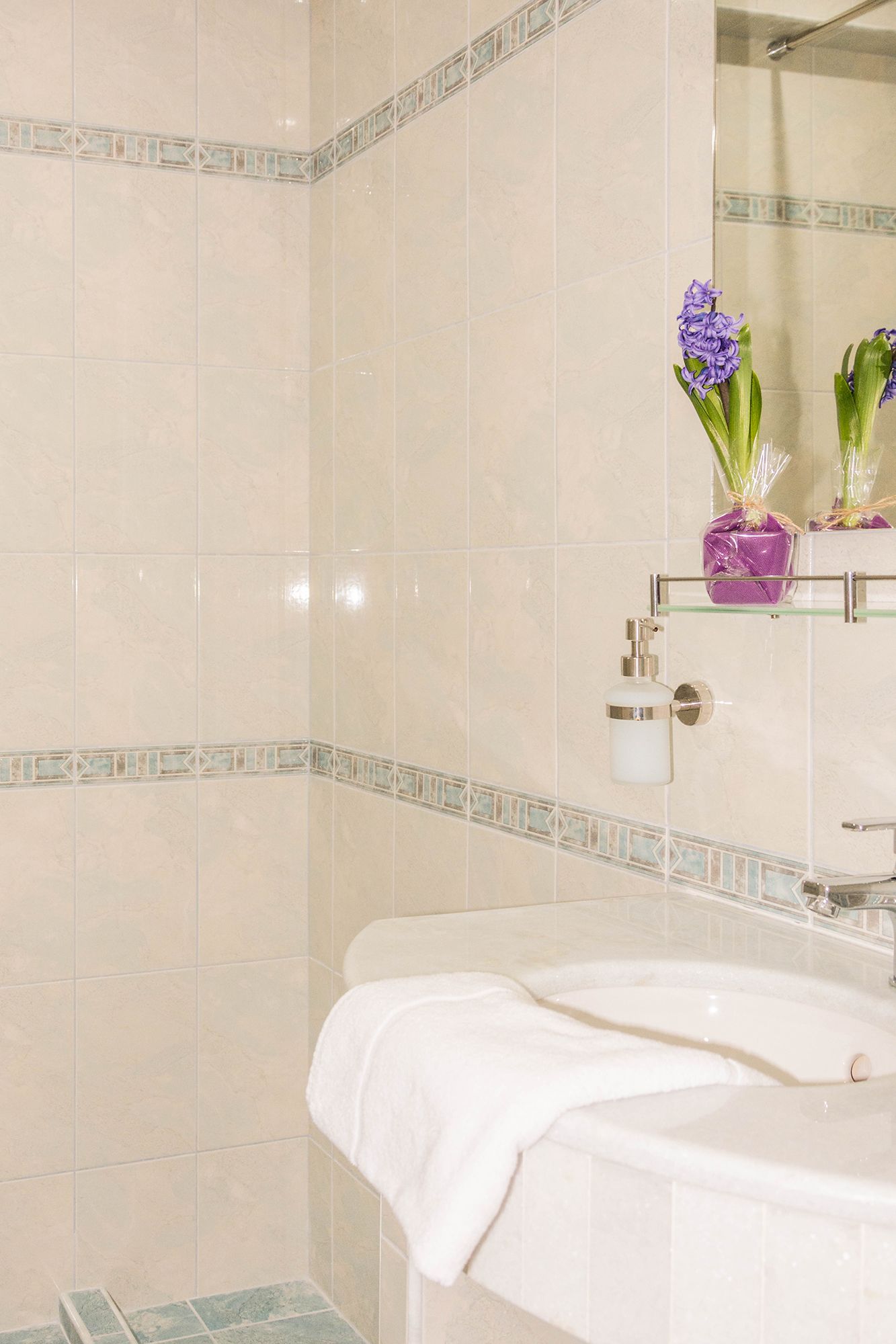 Ein Badezimmer mit einem weißen Waschbecken, einer Glastrennwand mit Blumen und einem Spiegel.
