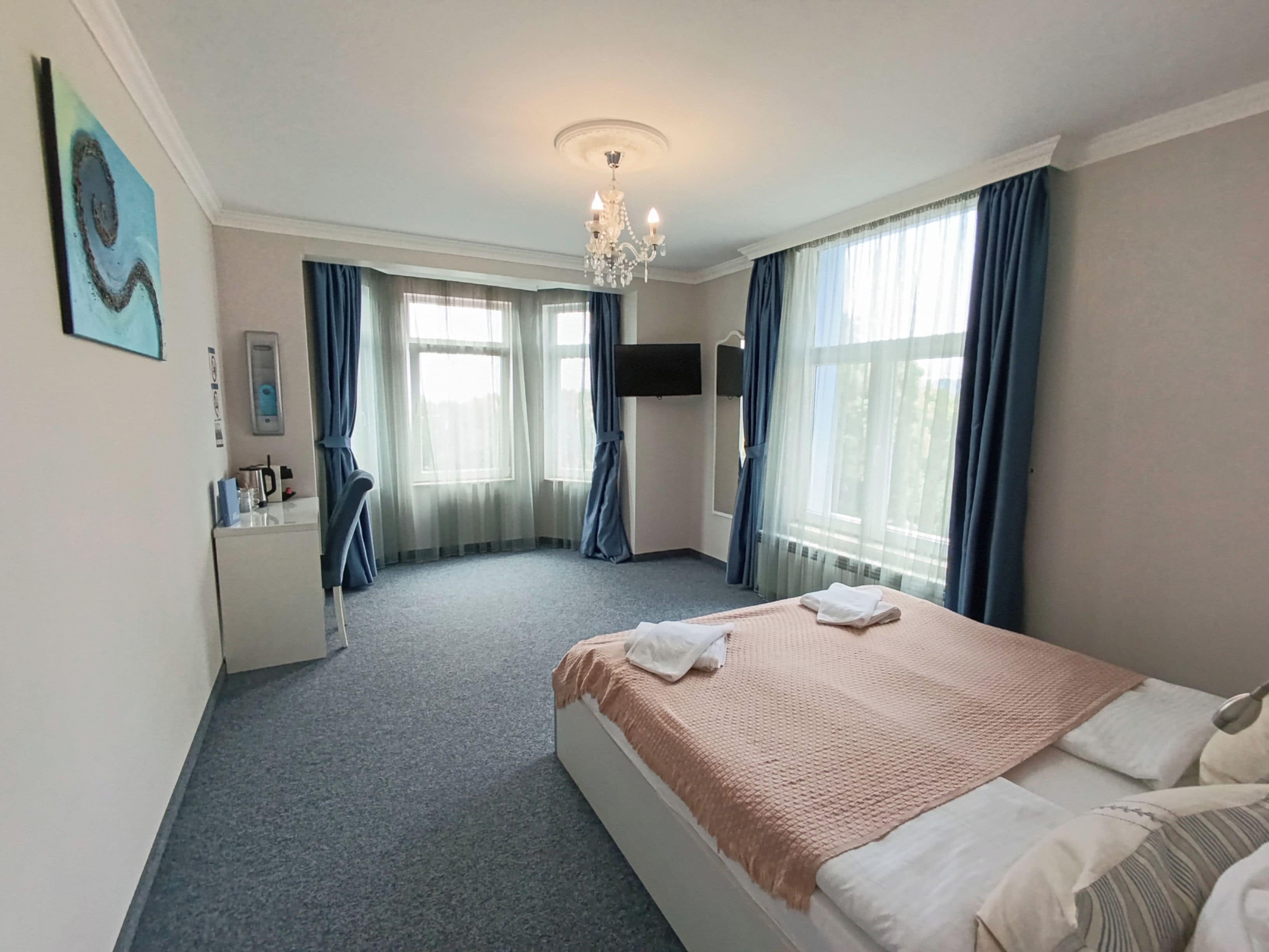 A hotel room with a bed, a desk, a chair, a TV, and a window with curtains.