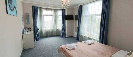 A hotel room with a bed, a desk, a chair, a TV, and a window with curtains.
