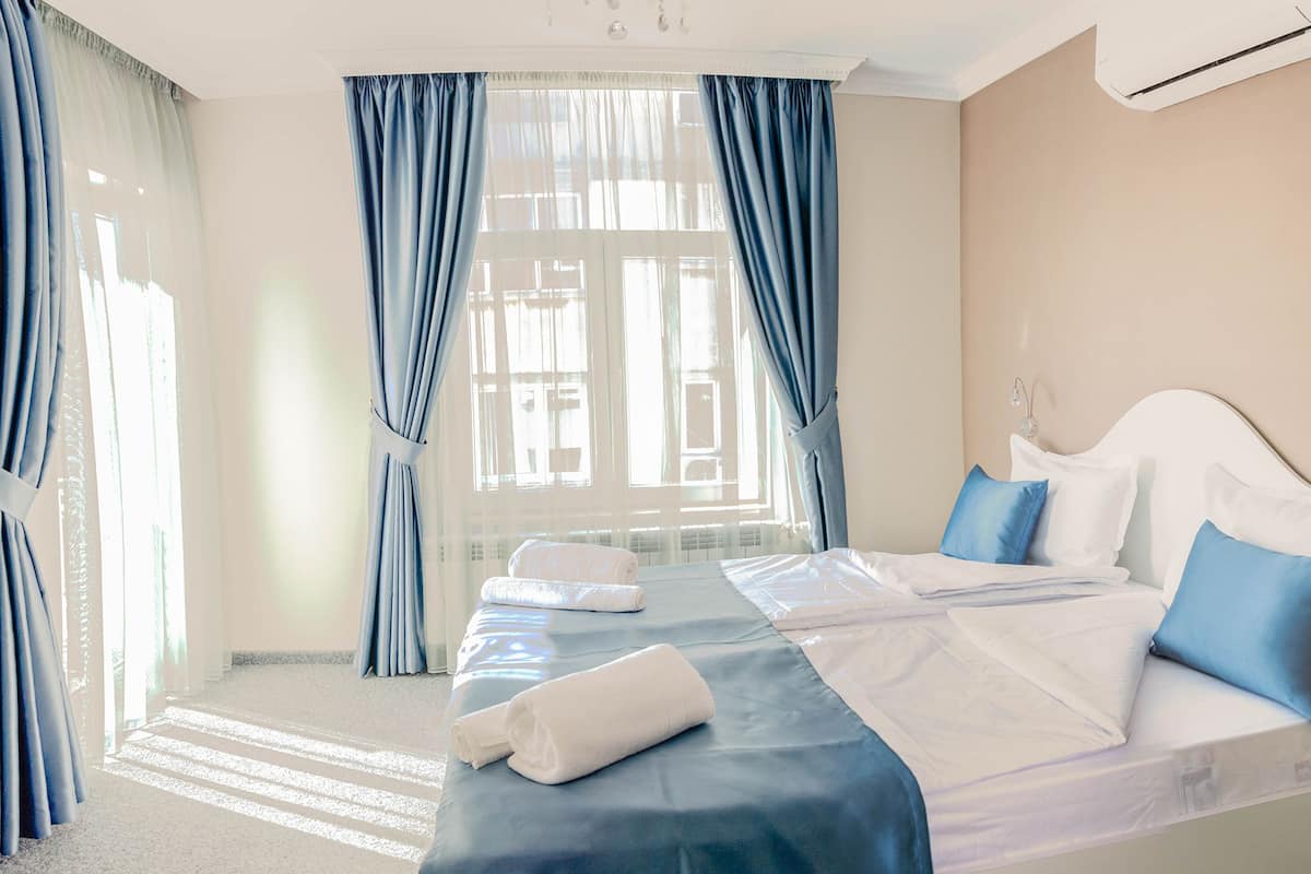 Una habitación de hotel con una cama grande, dos almohadas, una mesita de noche y un ventanal con cortinas.