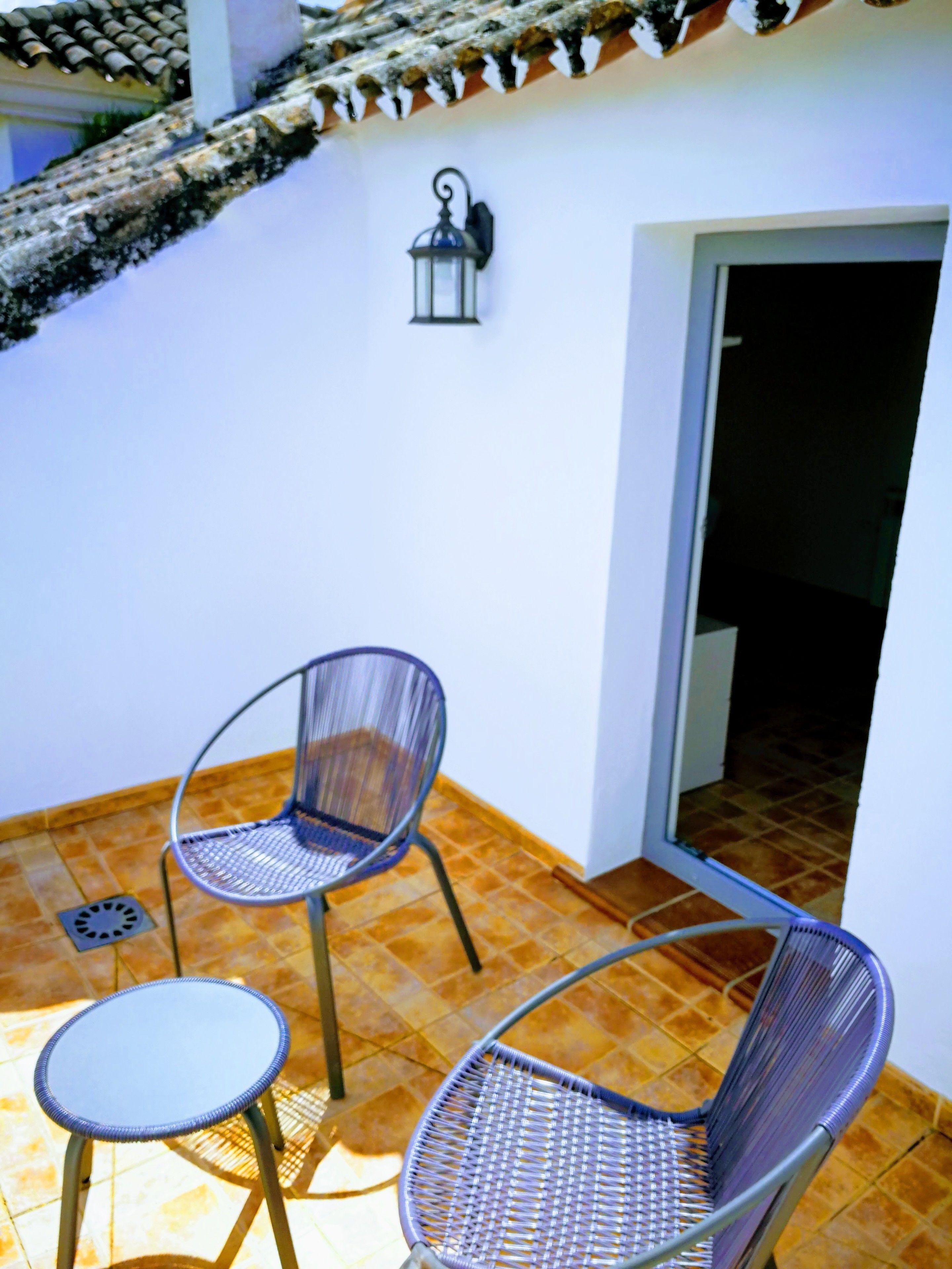 A patio with two chairs and a small table, a lantern, and a tiled floor.