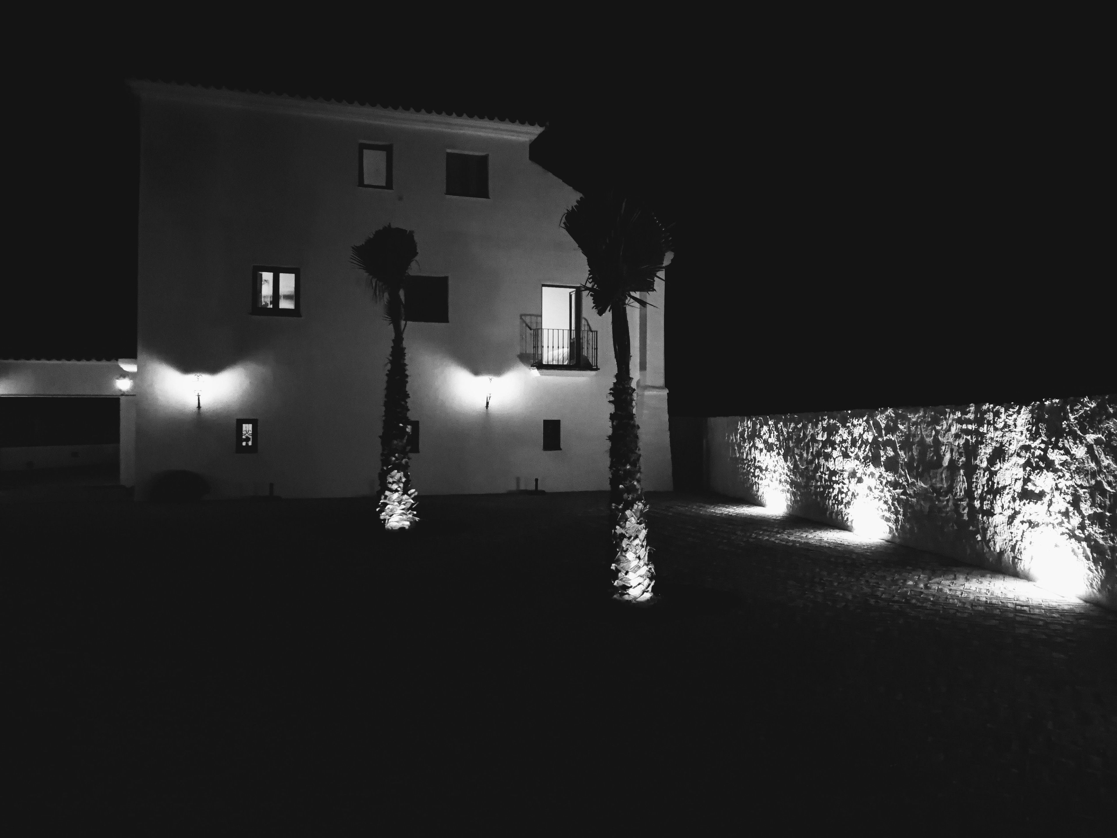 A building at night with illuminated windows and a well-lit garden area.
