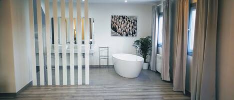 A modern bathroom with a freestanding bathtub, a large mirror, and a potted plant.