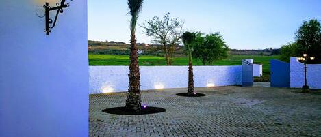 A paved courtyard with a white wall, a palm tree, and a lamp post.