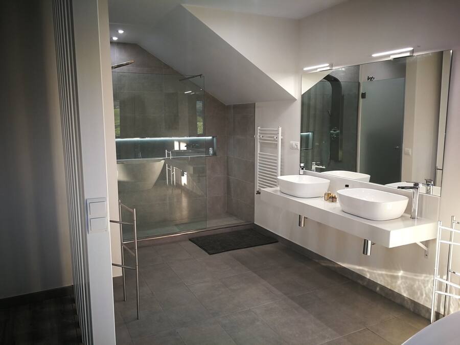 Un baño moderno con ducha a nivel del suelo, dos lavamanos y un espejo grande.