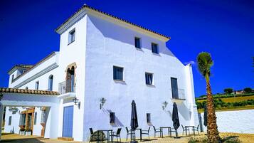 Un edificio blanco con tejado de tejas, numerosas ventanas y mesas exteriores con sombrillas.