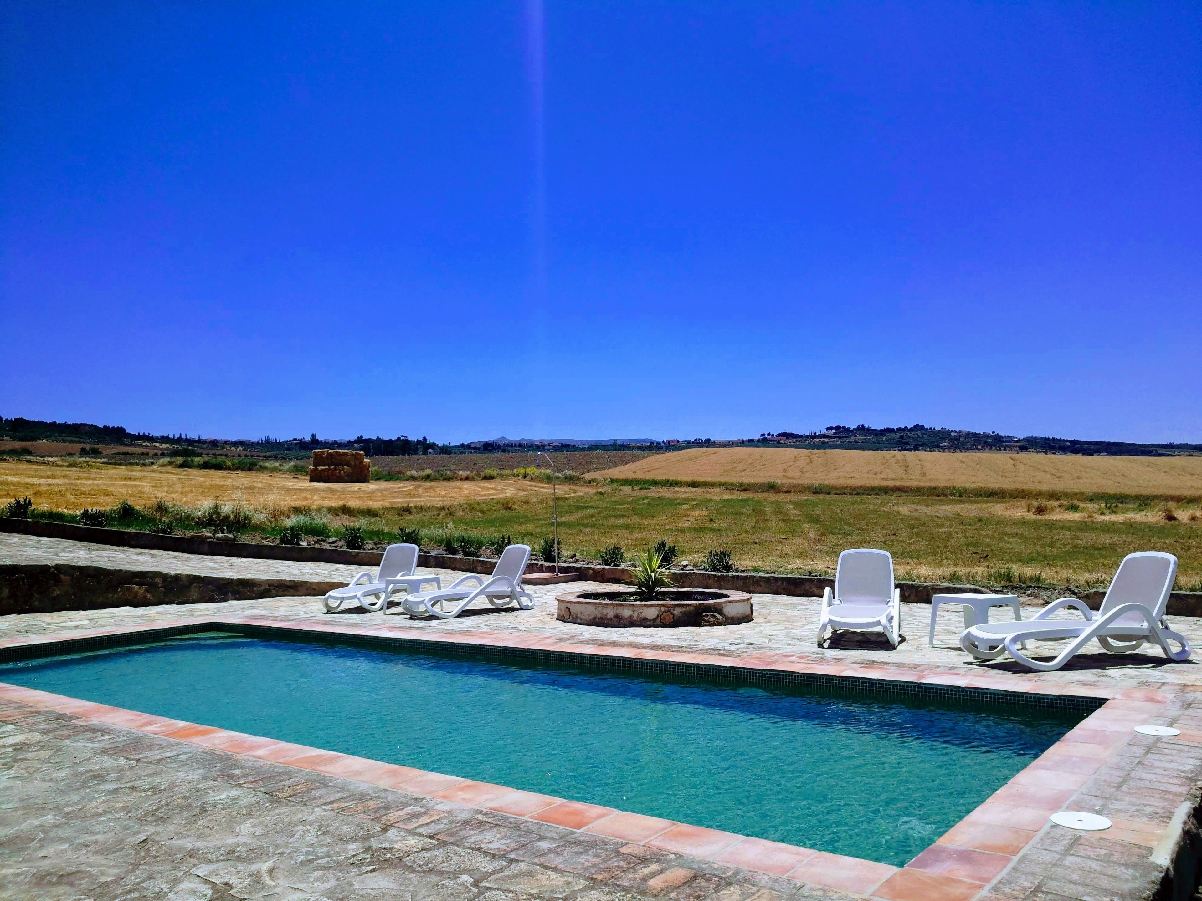 A swimming pool with lounge chairs and a view of a hilly landscape.