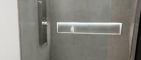 Una ducha moderna con puerta de vidrio, cabezal de ducha de mano y dispensador de jabón integrado.