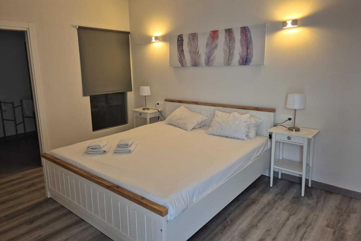A neatly arranged hotel room with a large bed, two bedside tables, a wall-mounted artwork, and a window with a blind.