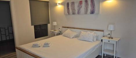A neatly arranged hotel room with a large bed, two bedside tables, a wall-mounted artwork, and a window with a blind.