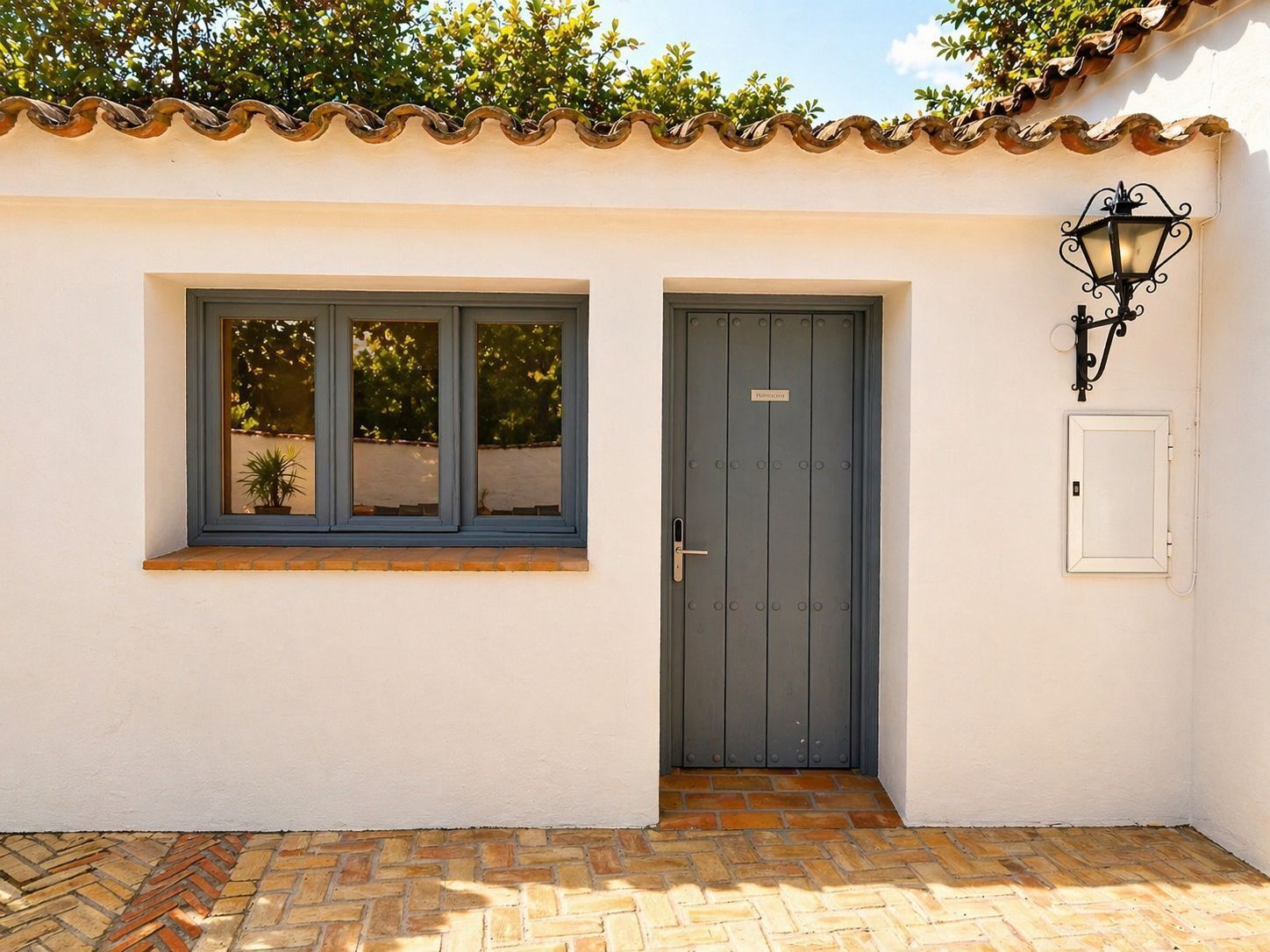 A building with a tiled roof, a door with a nameplate, a window with a view, and a wall-mounted light fixture.
