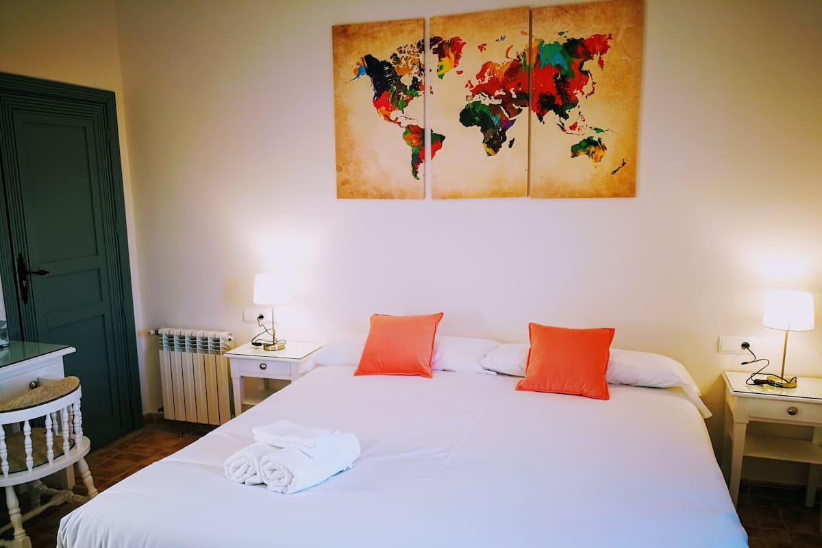A hotel room with a large bed, two nightstands with lamps, a map artwork on the wall, and a green door.
