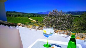 Een tafel met een glas water, een fles en een schaal met noten op een balkon met uitzicht op een prachtig landschap.