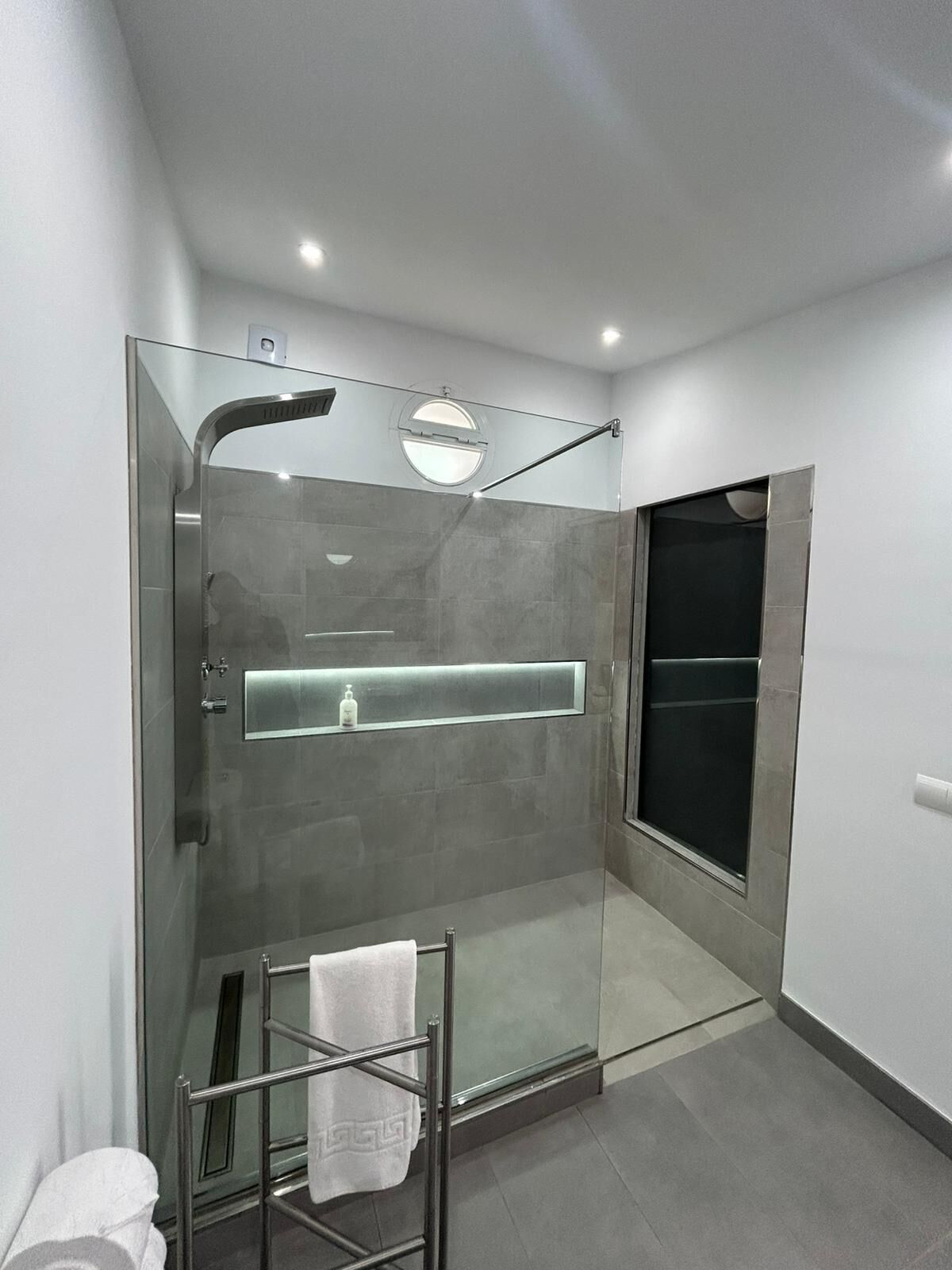 Un baño moderno con ducha acristalada, repisa de vidrio y un perchero para toallas.