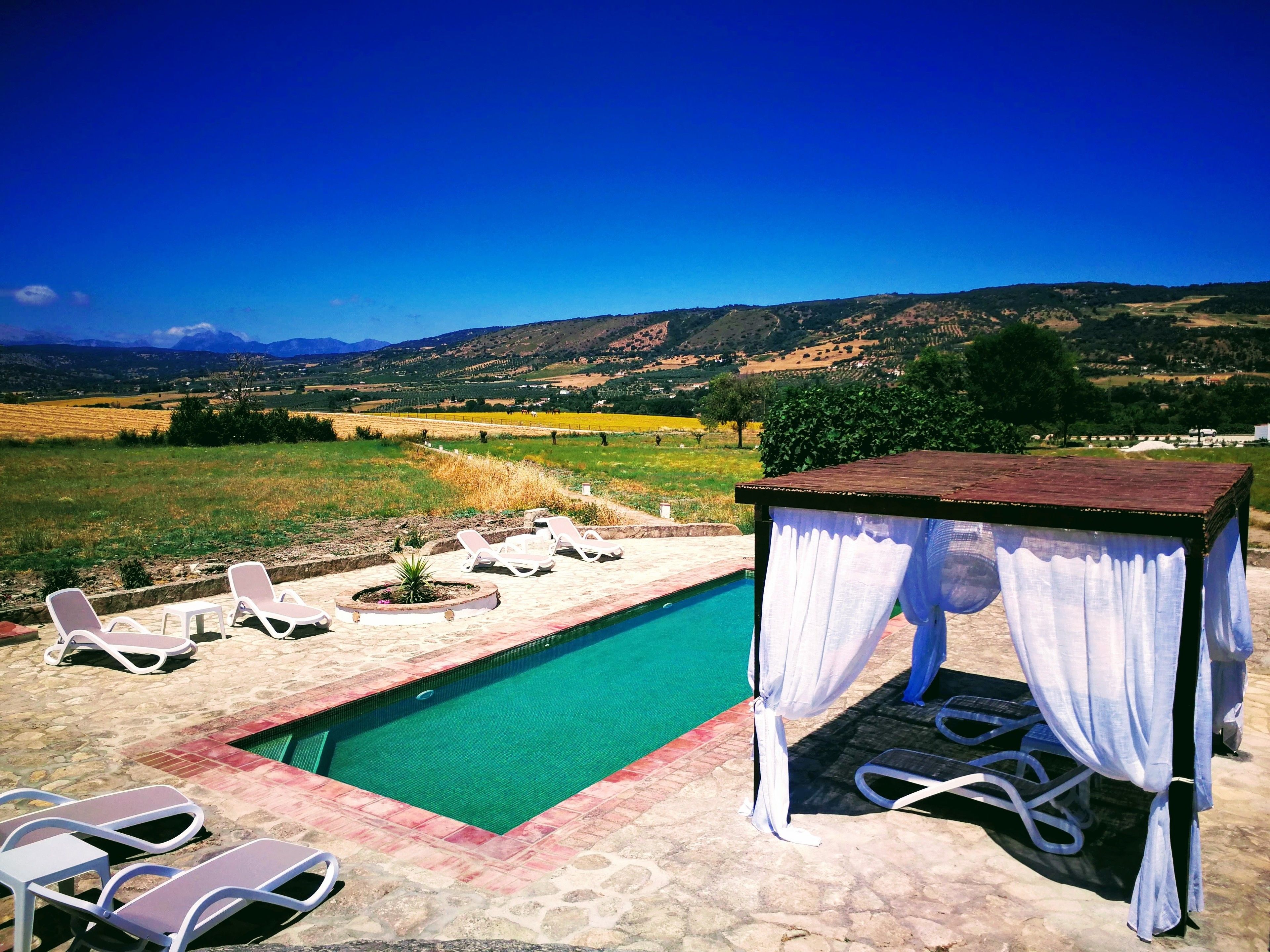 Ein Poolbereich mit Liegestühlen und einer Laube mit Blick auf eine malerische Landschaft.