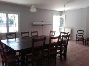 A dining room with a large rectangular table, six wooden chairs, two pendant lights, and a window with a view of trees. - Prato Plage (Pernes-les-Fontaines)