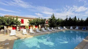 Una piscina con sillones blancos y un edificio con contraventanas rojas al fondo.