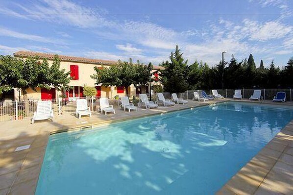 A swimming pool with white lounge chairs and a building with red shutters in the background. - Prato Plage (Pernes-les-Fontaines)
