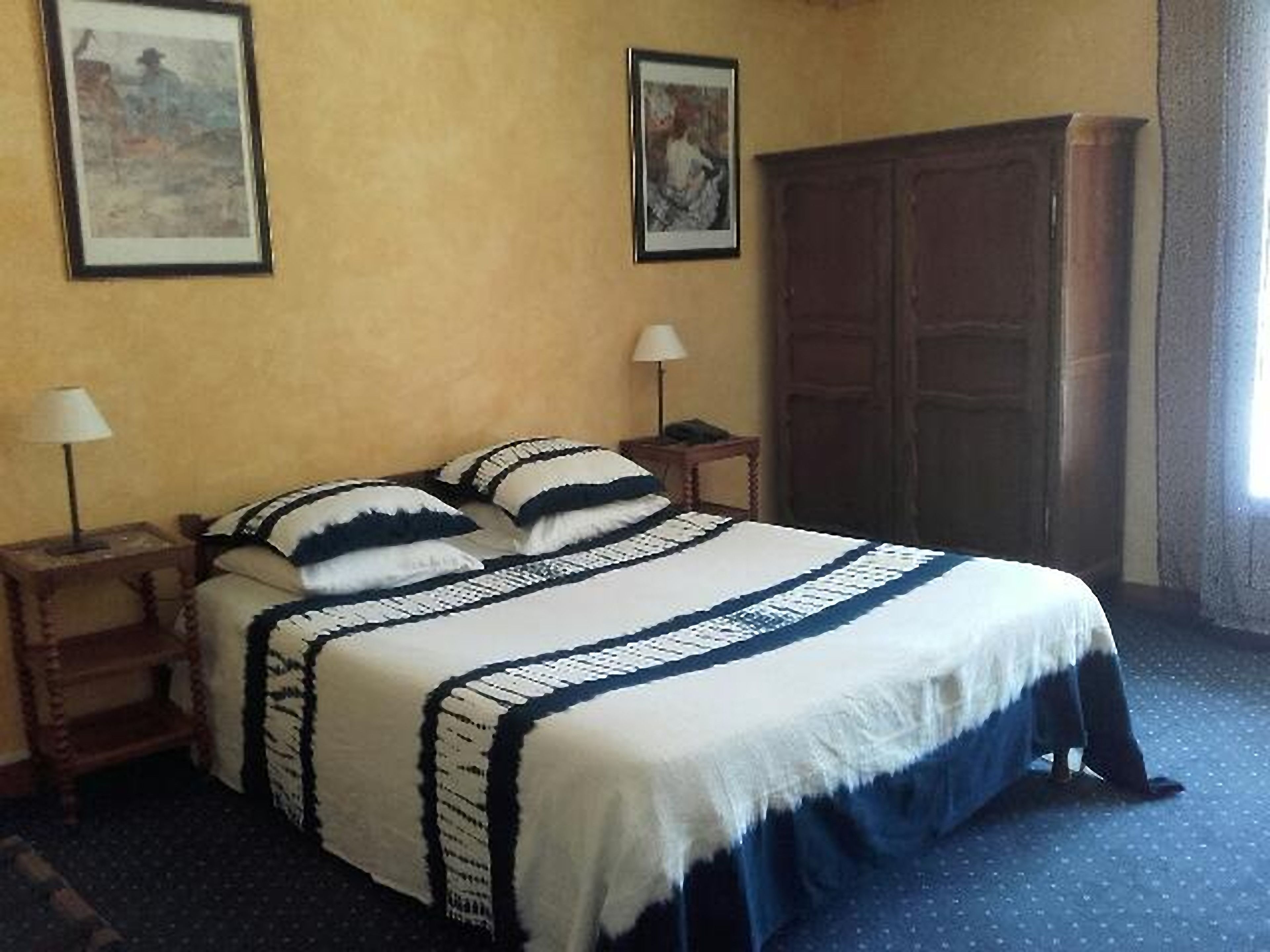 A hotel room with a bed, two bedside tables with lamps, a wardrobe, and two framed pictures on the wall.