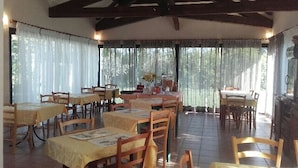 Un comedor con varias mesas y sillas, ventanas amplias con cortinas, y un techo alto con vigas a la vista.
