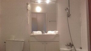 Un baño pequeño y funcional con inodoro, lavabo con espejo y zona de ducha.