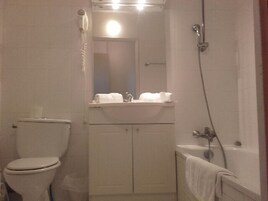 Une petite salle de bain compacte, comprenant des toilettes, un lavabo avec un miroir au-dessus, et un espace douche.