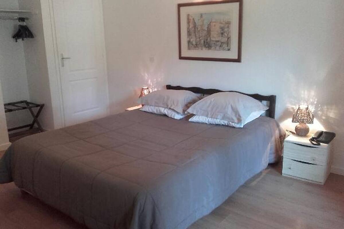 A bedroom with a bed, bedside lamps, a nightstand, a framed picture on the wall, and a door.