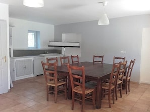 A dining area with a rectangular table surrounded by wooden chairs, a kitchen area with white cabinets, and a window providing natural light.