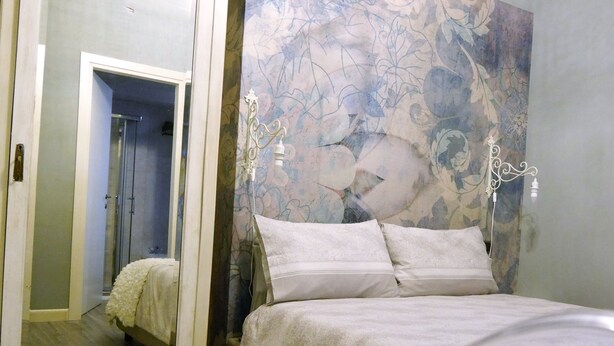 Un dormitorio con cama, espejo y pared con estampado floral.