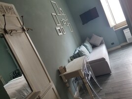 A room with a bed, a sofa, a table, and a wall-mounted TV.
