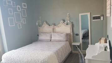 A bedroom with a bed, a bedside table, a dresser, and a mirror.