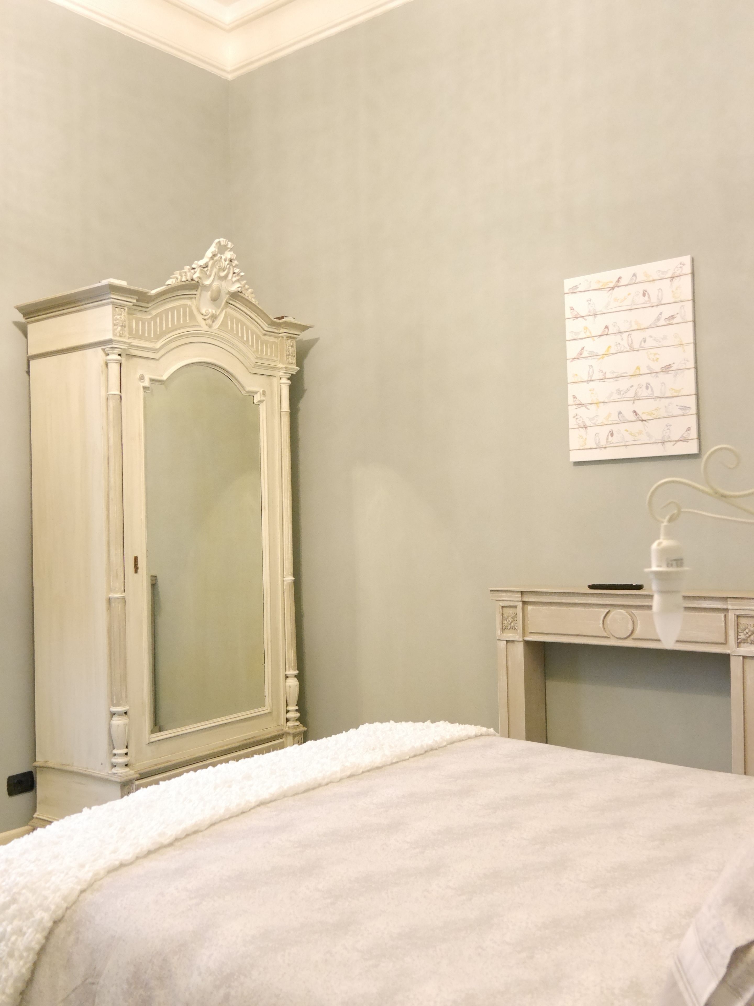 A bedroom with a large mirror, a bedside table, and a wall-mounted bird illustration.