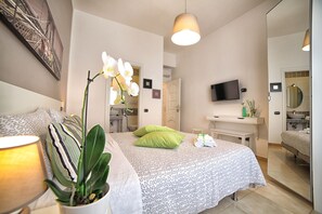 Un dormitorio moderno con una cama, una orquídea en maceta, un televisor y un espejo.