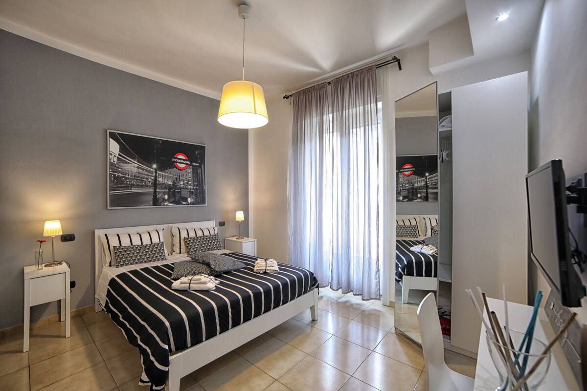 Ein modernes Schlafzimmer mit einem Bett, Nachttischen, einem Spiegel und einem großen Fenster mit Vorhängen.