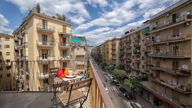 A multi-story residential building with balconies, a street view, and a clear sky. - City Central (Salerno)