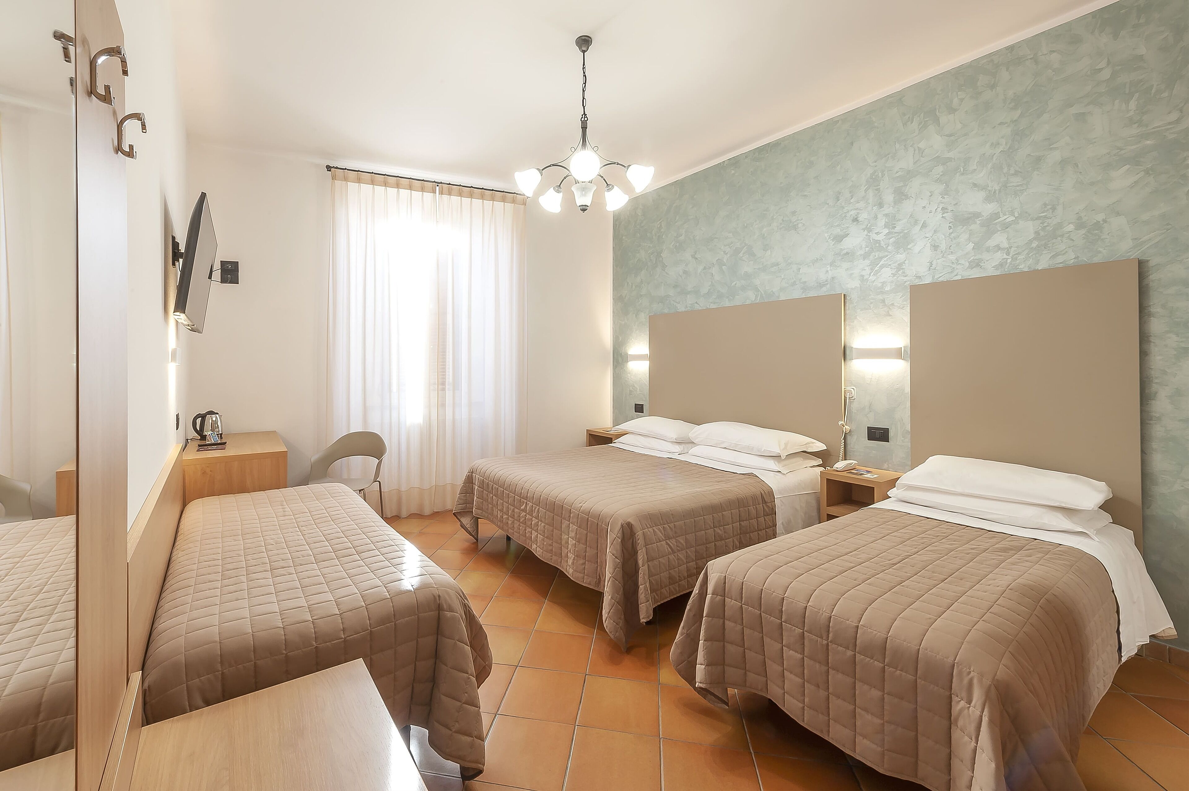 A hotel room with two beds, a desk, a chair, a mirror, and a window with curtains.