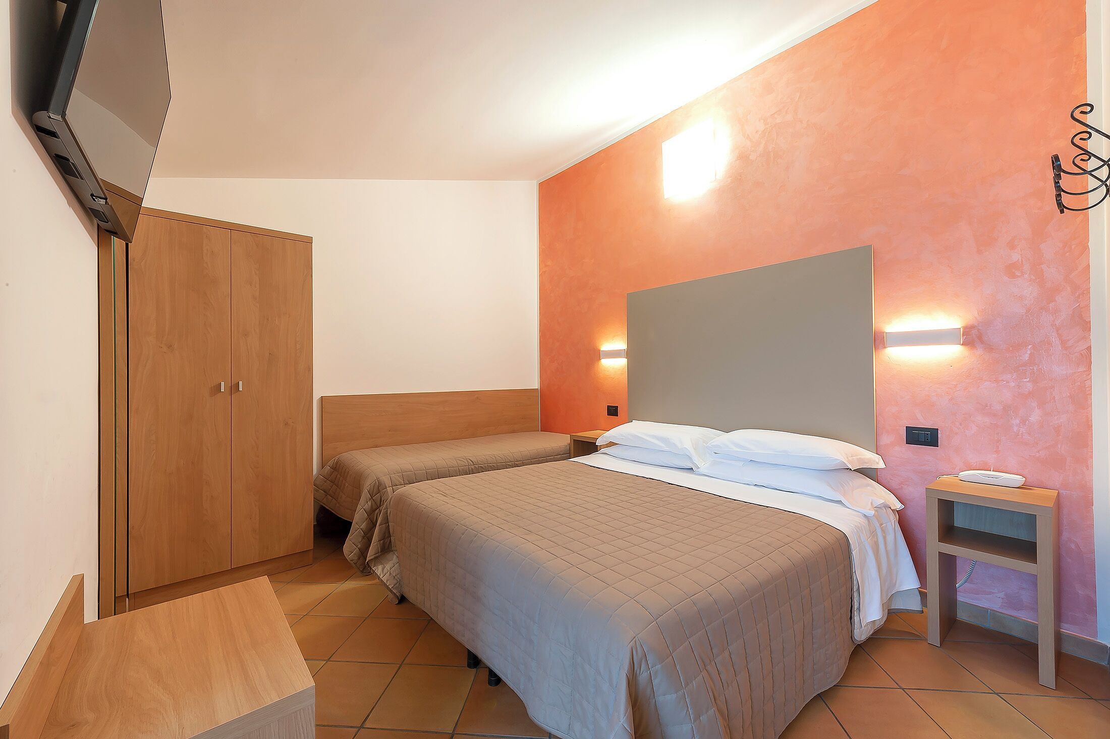 Ein Schlafzimmer mit zwei Betten, einem Kleiderschrank, einem Nachttisch und einem an der Wand befestigten Fernseher.