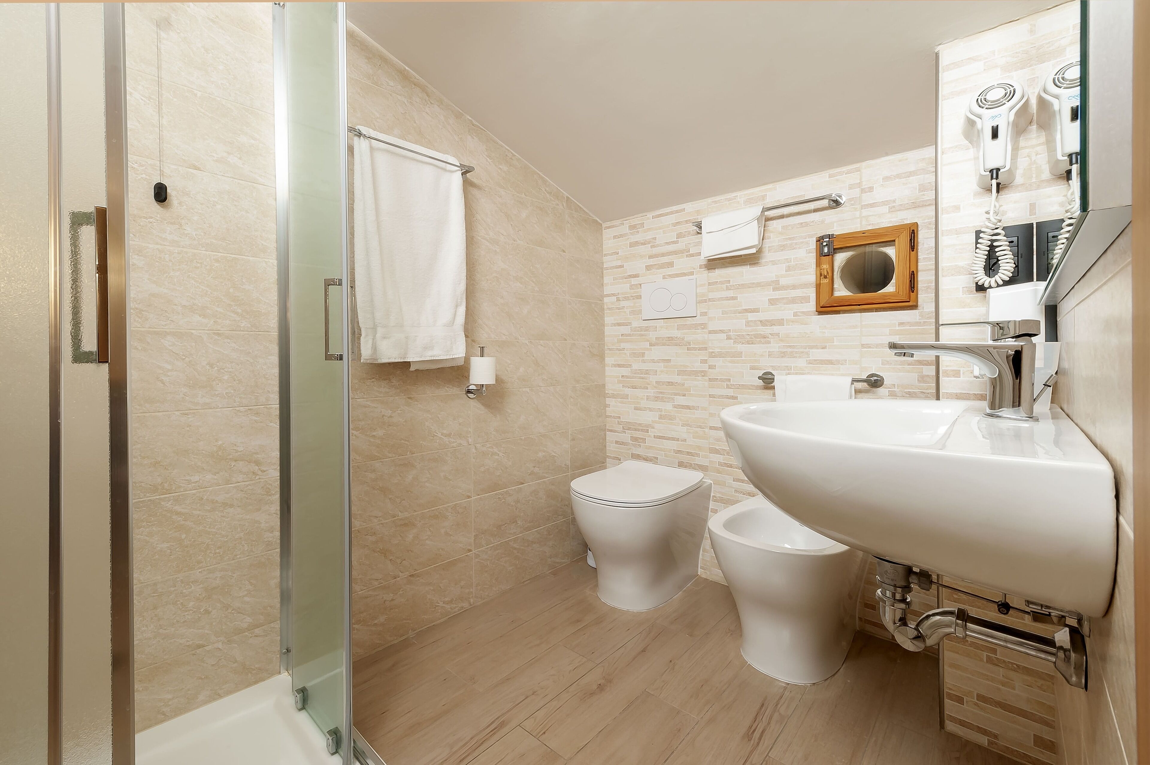 A modern bathroom with a glass shower enclosure, a white sink, and two toilets.